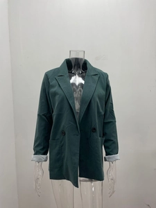 Detail of dark green blazer showing lapel collar, black buttons, and contrast grey lining sleeves