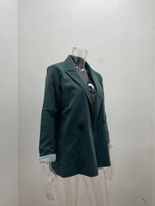 Detail showing the dark green blazer's lapel, black buttons, and textured fabric finish