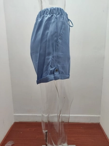 Dettaglio degli shorts azzurri con vita elastica a coulisse e orlo risvoltato con bottone