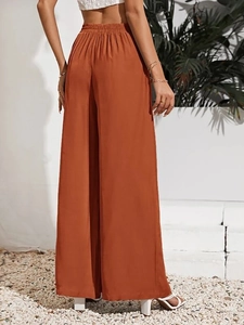 Dettaglio dei pantaloni a gamba larga rosso ruggine a vita alta con elastico e drappeggio fluido