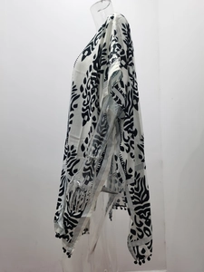 Détail du kimono bohème blanc avec feuilles tropicales noires et pompons décoratifs