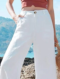 Dettaglio dei pantaloni in lino bianco a vita alta e gamba larga con bottone ambrato
