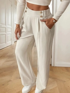 Detail of high waist cream trousers featuring elegant gold buttons and side pocket texture