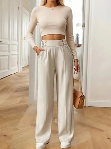 Detail of high waisted trousers with metal double buckles and pleats in cream beige color