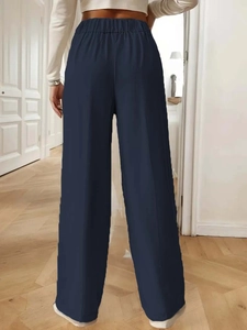 Rear view of model wearing high-waisted wide-leg navy trousers with elegant drape and elastic waist