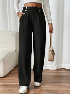 Detail view of high-waist black trousers featuring gold button accents and premium fabric