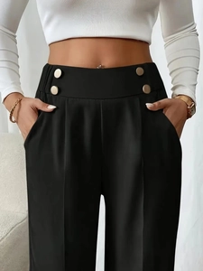 Detail of high waist trousers with four decorative gold buttons and sharp front pleats
