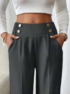 Detail view of high waisted dark grey trousers featuring decorative gold buttons on the waist