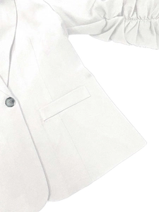 Dettaglio di blazer bianco con risvolto classico, bottone singolo e maniche arricciate