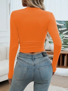 Macro view of bright orange long sleeve cropped tee with pleated side details and round neck