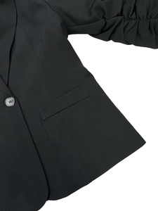 Dettaglio delle maniche arricciate e del bottone marmorizzato su blazer nero da donna