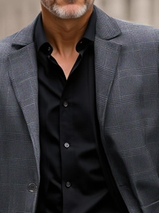 Detailed view of dark grey plaid suit lapel with smooth black dress shirt and resin buttons