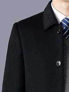 Détail du revers d'un manteau noir en laine avec gilet de costume et cravate rayée