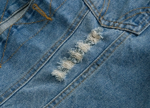 Detailed close-up of distressed blue denim fabric with horizontal ripped texture and orange stitching