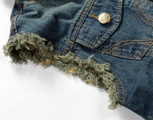 Detail of distressed frayed edge on denim vest with golden button and contrast stitching