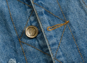 Detail of blue denim fabric with orange diamond stitching and engraved vintage metal button