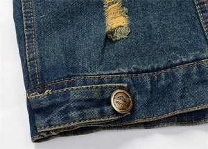 Detailed macro view of blue distressed denim fabric with ripped texture and brass button