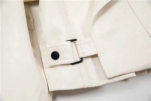 Close-up of adjustable side buckle and matte button on off-white leather jacket