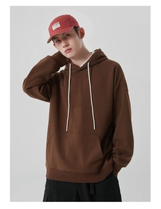Détail d'un sweat à capuche marron surdimensionné avec cordons blancs et poche kangourou devant