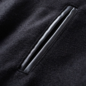 Detail of wool blend fabric and leather-trimmed pocket on a black varsity jacket