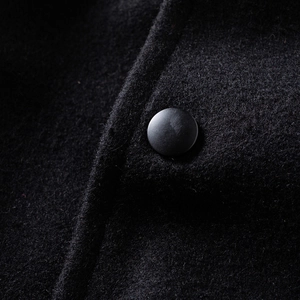 Close-up of black wool fabric texture with a matte button on a varsity jacket
