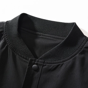 Detail of high-density ribbed knit collar and matte metal snap button on black bomber jacket