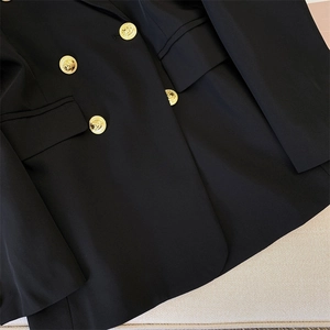 Detailed close-up of golden Medusa embossed buttons on a black double-breasted blazer jacket