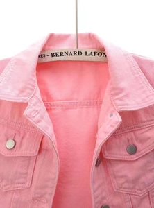 Detailed close-up of pink denim jacket collar with flap pockets and metal buttons