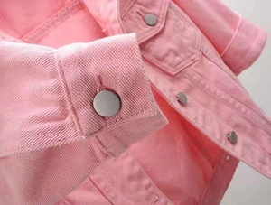 Detailed close-up of pink denim jacket fabric texture and silver metal buttons