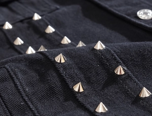 Close-up of black denim vest featuring silver conical studs and metal button detail