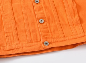 Detail of metal button with NEW JEANS engraving on vibrant orange denim jacket fabric