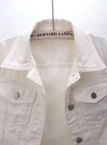 Detail of white denim jacket featuring metal buttons, classic lapels and chest pockets