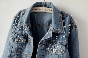 Detailed view of white faux pearls embellishment on light blue denim jacket collar