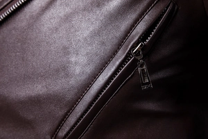 Macro detail of dark brown leather jacket featuring lychee grain texture and metal zipper