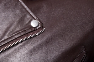 Detailed macro shot of dark brown leather jacket with silver zipper and metal snaps