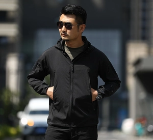 Outdoor street photo of a men's black tactical softshell jacket with hood and arm pockets