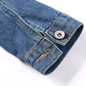 Gros plan du poignet d'une veste en jean bleue avec bouton en métal et coutures jaunes