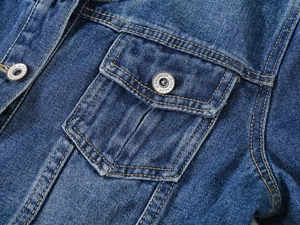 Détail de la poche poitrine en jean bleu avec coutures jaunes et bouton en métal gravé
