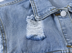 Gros plan détaillé d'un gilet en jean bleu clair avec bords effilochés et bouton argent