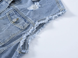 Détail du gilet en jean bleu clair avec des trous usés et des bords effilochés aux épaules