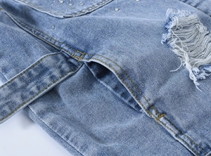 Détail du tissu denim bleu clair avec strass étincelants et zone usée avec franges blanches