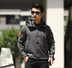 Detail of grey tactical softshell jacket with red star patch and multiple zipper pockets