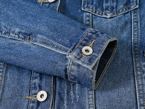 Détail du poignet d'une veste en jean bleu foncé avec coutures et bouton en métal