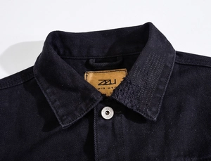 Close-up of black denim jacket with silver metal button and premium leather brand label