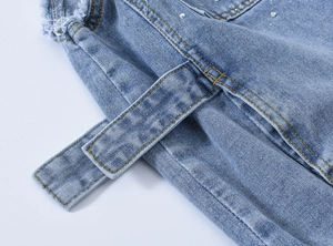 Détail de veste en jean bleu clair avec strass, bords effilochés et surpiqûres jaunes