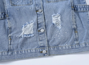 Détail du gilet en jean bleu clair avec boutons métalliques, trous usés et strass étincelants
