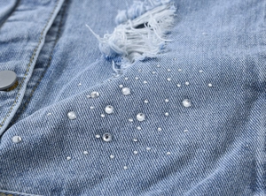 Détail d'un gilet en jean bleu clair montrant des trous usés et des strass étincelants