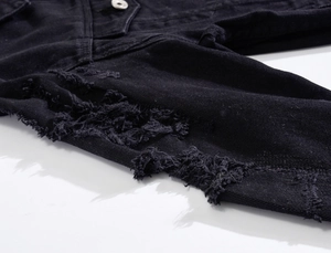 Close-up of distressed ripped details and metal button on black denim jacket