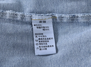 Gros plan sur l'étiquette d'entretien montrant 80% coton sur gilet en jean bleu clair