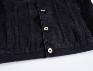 Close-up of black denim jacket metal buttons and pleated placket with visible twill texture